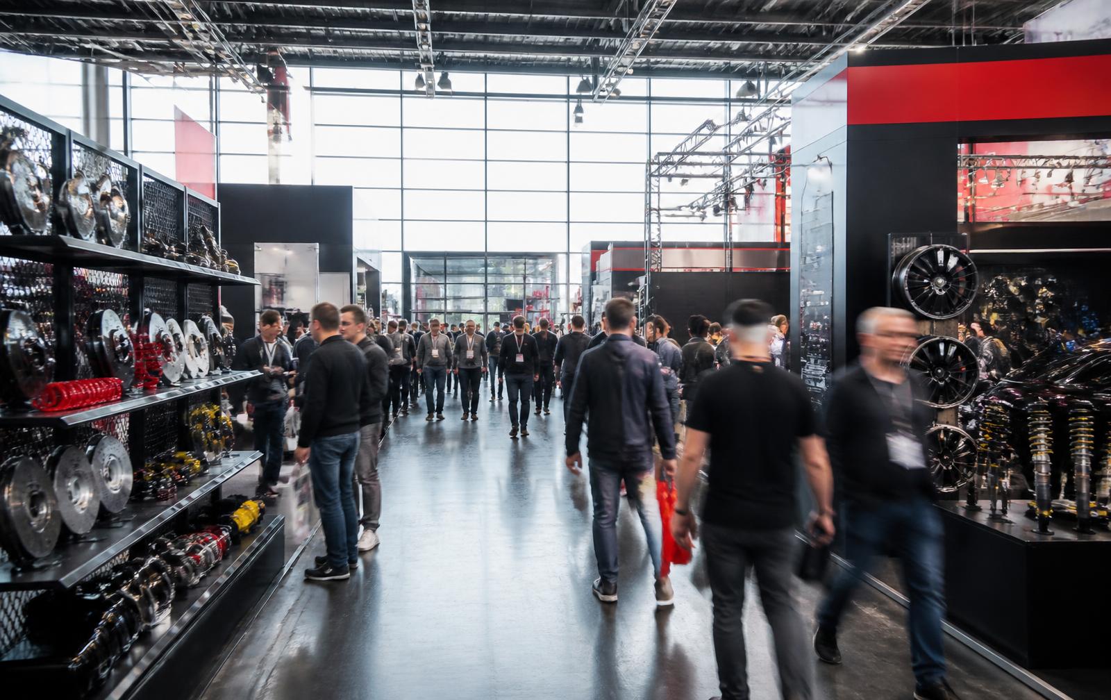 Besucherinnen und Besucher zwischen Messeständen mit Fahrzeugteilen auf einer Automotive-Fachmesse